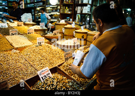 Noci in vendita al Bazar delle Spezie di Istanbul, Turchia | ISTANBUL, Turchia — Cassette di legno piene di noci, frutta secca e legumi delimitano uno stand all’interno del Bazar delle Spezie a Eminönü, parte del commercio di prodotti sfusi che ha definito il Bazar Egiziano dalla sua costruzione nei primi anni ’1660. Il nome turco del mercato, Mısır Çarşısı, che significa „Mercato Egiziano“, riflette sia le entrate fiscali egiziane che hanno contribuito a finanziare la moschea Yeni Cami adiacente, sia le merci che un tempo arrivavano attraverso rotte egiziane. Foto Stock