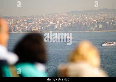 Spedizione sul Bosforo dal Palazzo Topkapi di Istanbul // ISTANBUL, Turchia - la vista della spedizione sul Bosforo dal Palazzo Topkapi con turisti in primo piano. Una grande nave da carico e un traghetto passeggeri più piccolo navigano lungo lo stretto affollato, con l'immensa città di Istanbul visibile sulla costa lontana. Foto Stock