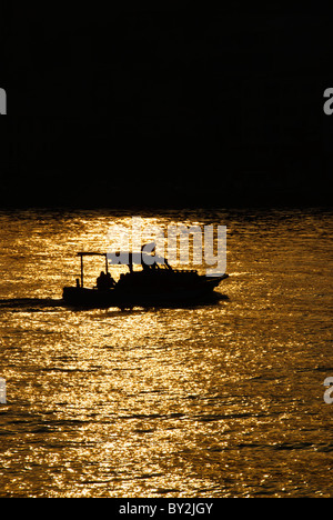 ISTANBUL, Turchia / Türkiye / Türkiye - Una piccola barca da pesca si staglia contro le scintillanti acque del Bosforo durante un tramonto dorato a Istanbul, Turchia. Il Bosforo, una via d'acqua vitale che collega il Mar Nero al Mar di Marmara, offre splendide scene di Istanbul con i suoi monumenti storici e la vivace attività marittima. Questo iconico stretto divide la città in lati europei e asiatici, con splendidi palazzi sul lungomare, moschee e ponti. Foto Stock