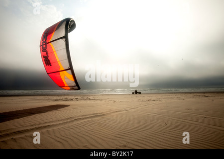 Silhouette di un maschio kite buggier (kite buggy) che rotolano lungo la spiaggia di inquietanti nubi e luce insolita. Foto Stock