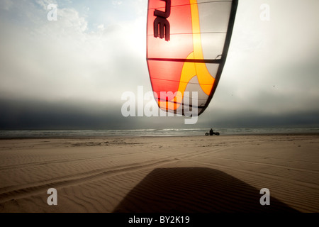 Silhouette di un maschio kite buggier (kite buggy) che rotolano lungo la spiaggia di inquietanti nubi e luce insolita. Foto Stock