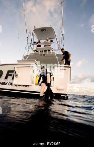 Una donna si siede sul bordo di una barca di immersione della porta, preparando per un tuffo nelle acque della Costa Rica. Foto Stock