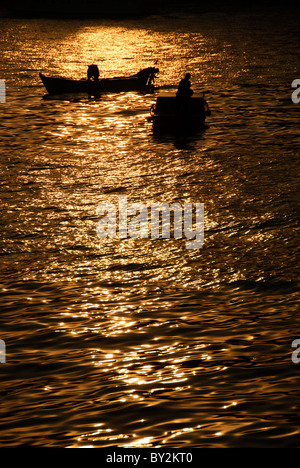 Barche da pesca sagomate al tramonto sullo stretto del Bosforo Istanbul Turchia // ISTANBUL, Turchia - due piccole barche da pesca sono sagomate contro il riflesso del tramonto sul Bosforo a Istanbul, Turchia. Il Bosforo, una via d'acqua vitale che collega il Mar Nero al Mar di Marmara, offre splendide scene di Istanbul con i suoi monumenti storici e la vivace attività marittima. Questo iconico stretto divide la città in lati europei e asiatici, con splendidi palazzi sul lungomare, moschee e ponti. Foto Stock