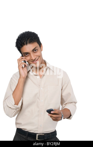 Un uomo che parla su un cellulare e tenendo premuto un altro rivolto verso la telecamera Foto Stock