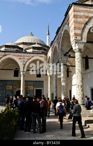 Palazzo Topkapi Harem turisti Istanbul // ISTANBUL, Turchia — turisti presso l'Harem del Palazzo Topkapi, il palazzo ottomano nel quartiere Sultanahmet di Istanbul. Lo storico cortile presenta imponenti colonnati ad arco, una grande cupola e intricate piastrelle, con i visitatori che esplorano l'ex residenza imperiale sotto un cielo limpido. Foto Stock