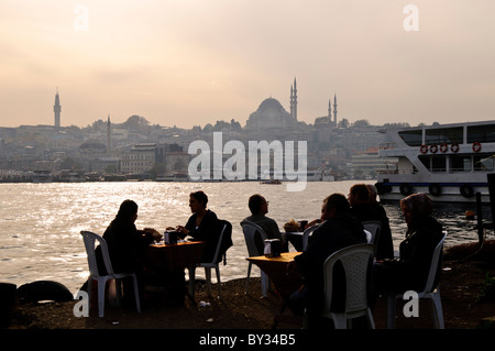 ISTANBUL, Turchia - i clienti possono gustare un pasto in un ristorante di pesce adiacente al mercato del pesce di Karakoy vicino al ponte Galata. La storica Moschea Suleymaniye, completata nel 1557, domina lo skyline attraverso il canale del Corno d'Oro. La moschea, la più grande dell'Impero Ottomano, esemplifica l'architettura ottomana classica. Foto Stock