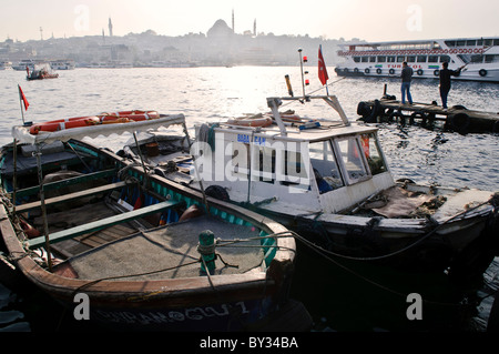 ISTANBUL, Turchia: Barche da pesca ormeggiate sul lungomare adiacente al mercato del pesce di Karakoy vicino al ponte Galata a Istanbul. La storica Moschea Suleymaniye, la più grande moschea dell'Impero Ottomano completata nel 1557, domina lo skyline attraverso il canale del Corno d'Oro. Queste navi da lavoro forniscono le catture giornaliere al vicino mercato ittico. Foto Stock