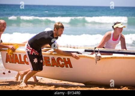 Uomini e donne che spingono una barca di salvataggio del surf del legno avalon, sydney, Australia Foto Stock