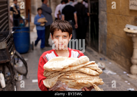 Ragazzo siriano che trasportano il pane fresco al di fuori del forno nella vecchia città di Aleppo, Siria Foto Stock