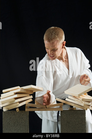 Giovane uomo schede di rottura con il karate chop su sfondo nero Foto Stock