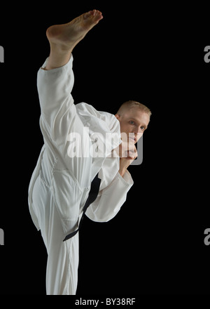 Giovane uomo eseguendo il karate kick su sfondo nero Foto Stock
