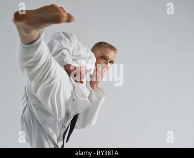 Giovane uomo eseguendo il karate kick su sfondo bianco Foto Stock