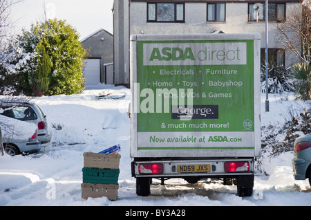 Regno Unito, Gran Bretagna. Asda home delivery van al di fuori di una casa offrendo lo shopping online con la neve sulla strada residenziale in inverno Foto Stock