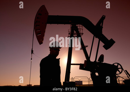 Silhouette di lavoratore di olio dalla pompa jack sul rig Foto Stock