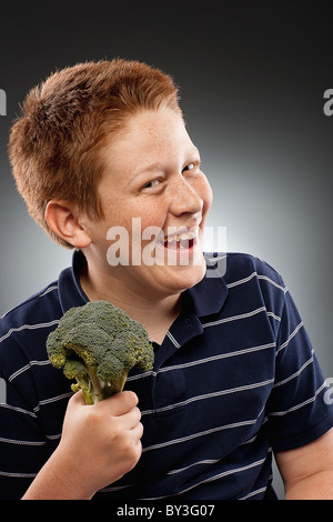 Ritratto di redhead ragazzo adolescente (14-15) tenendo i broccoli e ridere, studio shot Foto Stock