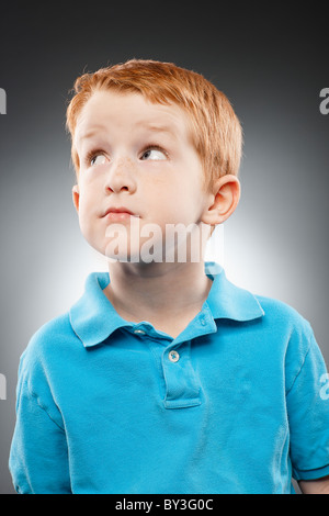 Ritratto di sorridere redhead ragazzo (4-5) indossando blue Polo shirt e guardando in alto, studio shot Foto Stock