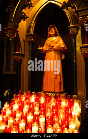 MONTREAL, Canada - Una scultura di Saint Marguerite Bourgeoys, accompagnata da candele votive, onora il primo insegnante di Montreal e fondatore della Congregazione di Notre Dame. Bourgeoys, che fondò la prima scuola della città nel 1658 e fu canonizzata nel 1982, rappresenta una figura significativa nel patrimonio educativo e religioso di Montreal. Lo spazio devozionale nella basilica di Notre-Dame invita alla preghiera e alla riflessione sul suo ruolo pionieristico nella Montreal coloniale. Foto Stock