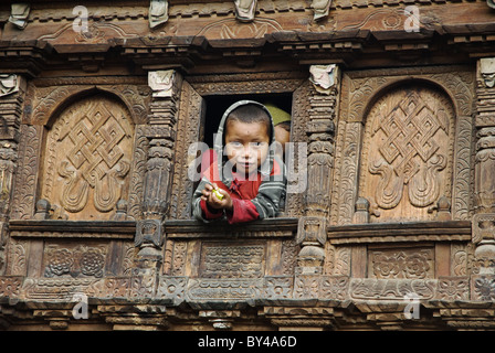 Un ragazzo Tamang orologi da una finestra in una riccamente intagliati casa in legno, Gatlang, Tamang Heritage trek, Nepal Foto Stock