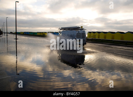 Cabine sulla spiaggia, riflesso in acqua di inondazione su una strada costiera Foto Stock