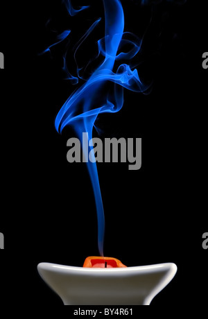 Fumo blu passando da un arancione spenta candela in un piatto su un sfondo nero Foto Stock