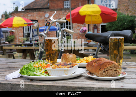 Due ciclisti si fermano per un gustoso pranzo e un po' di lager nel giardino dei pub di campagna del Flower Pot Hotel, Aston, Henley-on-Thames, Berkshire, UK Foto Stock