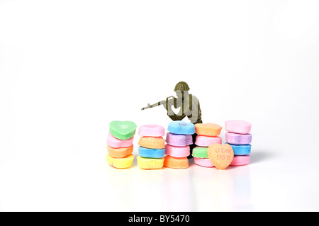 Un giocattolo di plastica soldato dietro una barricata di candy conversazione cuore caramelle prende la mira con il suo fucile. Foto Stock