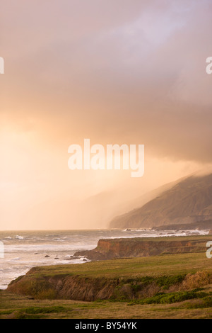 Un burrascoso Oceano Pacifico si blocca contro la costa rocciosa della California centrale lungo la Pacific Coast highway al tramonto, San Simeone. Foto Stock