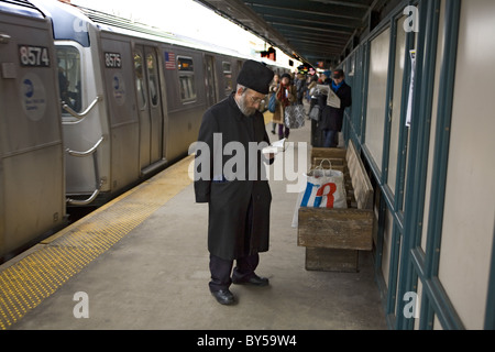 Ebrea ortodossa uomo dice preghiere sulla piattaforma della metropolitana come il treno entra nella stazione di Williamsburg, Brooklyn, New York Foto Stock