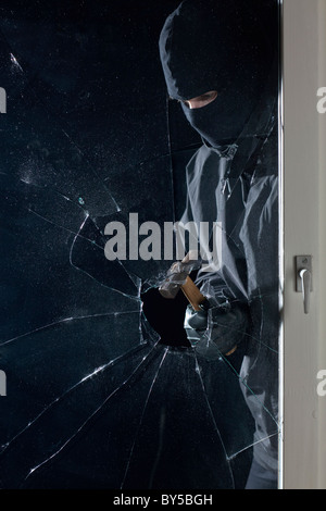 Un criminale la rottura in una finestra con un martello Foto Stock