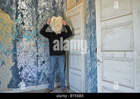 Figura maschile oscurata dalla carta da parati strappata shred in casa abbandonata interni. Foto Stock