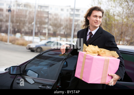 Ritratto di happy businessman camminare al di fuori della sua vettura con grande giftbox in mano Foto Stock