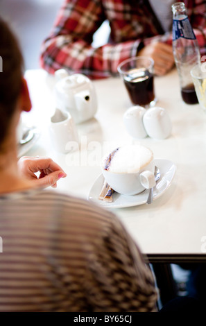 Una coppia di amici seduti in un bar con bevande di socializzare. Il cappuccino è il punto di fuoco qui. Foto Stock