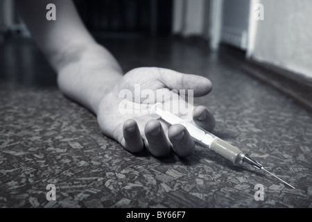 Mano di stupefacenti con la siringa sul pavimento. Foto in bianco e nero Foto Stock