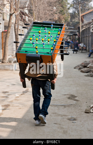 Uomo che porta Subbuteo® football soccer tavolo da gioco sul suo retro attraverso l'Hutong, Chengdu nella provincia di Sichuan, in Cina. JMH4408 Foto Stock