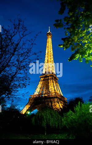 Torre Eiffel struttura di ferro illuminata d'oro contro il cielo notturno blu Parigi Francia // PARIGI, Francia - la Torre Eiffel è illuminata con luci dorate contro il cielo notturno della capitale francese. Progettata da Gustave Eiffel per l'esposizione mondiale del 1889, questa iconica struttura in ferro sul campo di Marte è uno dei monumenti a pagamento più visitati al mondo. La sua illuminazione dorata notturna, che include uno spettacolo di cinque minuti di luce scintillante ogni ora dopo il tramonto, crea un faro nel paesaggio notturno parigino. La torre è alta 330 metri (1.083 piedi), inclusa l'antenna. Foto Stock