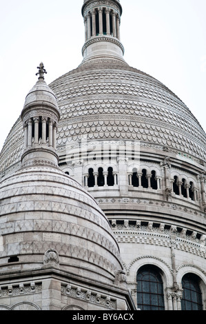 Basilica del Sacro Cuore Cupole Bianche Dettagli Architettonici Parigi Francia | PARIGI, Francia — Le cupole ravvicinate e le gallerie in pietra scolpita della Basilica del Sacro Cuore rivelano i dettagli fini applicati alla sua facciata romano-bizantina. Il motivo a conchiglia sulle piastrelle della cupola principale e la galleria ad arcate sotto di essa sono caratteristici del design dell'architetto Paul Abadie, completato nel 1914 con travertino pallido di Château-Landon. Foto Stock