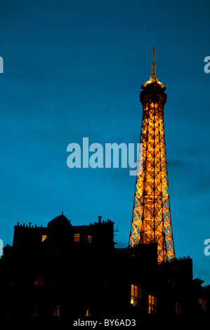 Torre Eiffel illuminata sopra edifici sagomati Parigi Francia // PARIGI, Francia - la Torre Eiffel, un'iconica struttura a reticolo di ferro, è illuminata contro un cielo crepuscolo, sagomata sopra gli edifici della capitale francese. Le sue luci iniziano a brillare mentre il giorno svanisce nella notte sopra Parigi, spesso chiamata la "città della luce". Progettata da Gustave Eiffel per l'esposizione universale del 1889, la torre è alta 330 metri (1.083 piedi), inclusa la sua antenna. Foto Stock