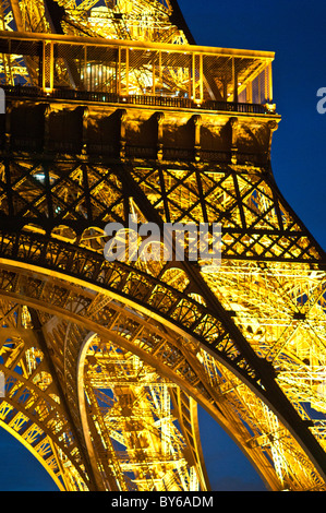 Torre Eiffel Struttura in ferro illuminata Dettaglio Luci dorate di notte Parigi Francia | PARIGI, Francia — Un primo piano delle inferriate del primo livello della Torre Eiffel brilla d'oro di notte, rivelando i nomi incisi di scienziati francesi tra cui Arago, Monge e Poisson posizionati sotto il balcone. Gustave Eiffel aggiunse il fregio di 72 scienziati, ingegneri e matematici come risposta ai critici che avevano denunciato la torre prima del suo completamento nel 1889. Foto Stock