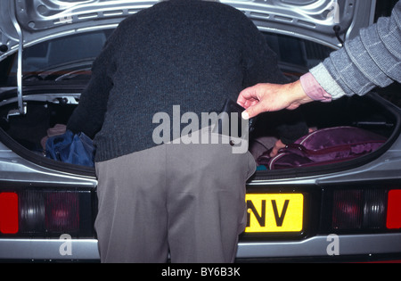 Pickpocket sollevamento di portafogli da uomo vecchio tasca posteriore nel parcheggio pubblico pur distratti cercando nel bagagliaio della vettura poste dai modelli England Regno Unito Foto Stock