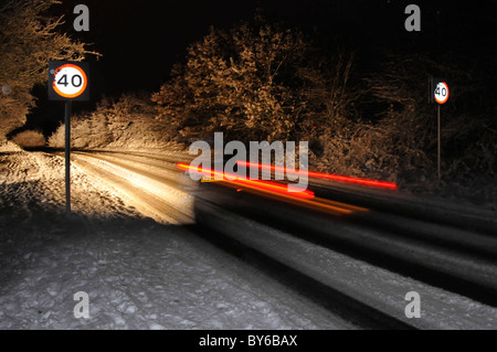 La guida su strade innevate di notte Foto Stock