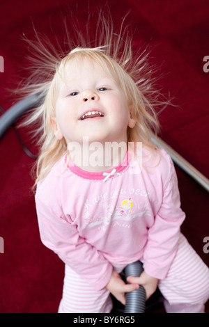 Bambina abiti rosa con capelli pungenti seduto su aspirapolvere sul tappeto rosso, Germania Foto Stock