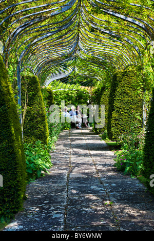 Tre persone sedute su un sedile in legno o banco in un angolo ombreggiato sotto una pergola in un paese di lingua inglese giardino d'estate. Foto Stock