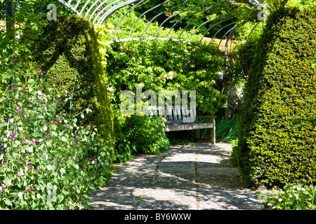 Sedile in legno o banco in un angolo ombreggiato sotto una pergola in un paese di lingua inglese giardino d'estate. Foto Stock