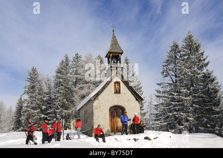 Persone di fronte alla cappella di escursioni invernali trail nel paesaggio innevato, Hemmersuppenalm, Reit im Winkl, Chiemgau, Baviera, Germania, Foto Stock