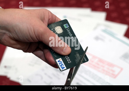 Qualcuno il taglio di una carta di credito con cambiali in background Foto Stock