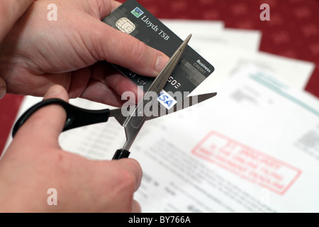 Qualcuno il taglio di una carta di credito con cambiali in background Foto Stock