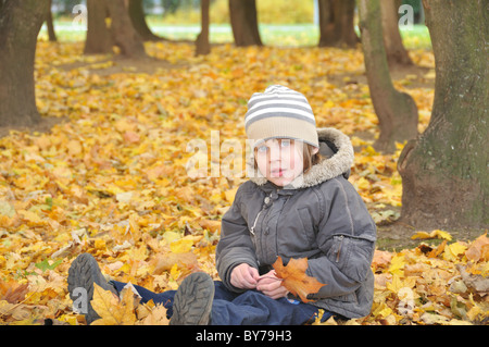 Ragazzo seduto in caduta foglie di giallo Foto Stock