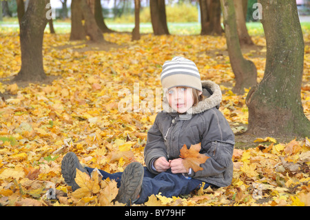 Ragazzo seduto in caduta foglie di giallo Foto Stock