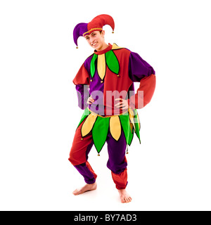 Scatto a tutta lunghezza di giovane maschio caucasico vestito come un Jester. Posa con le mani sui fianchi, ginocchia piegate, sorridente guardando la fotocamera. Sfondo bianco Foto Stock