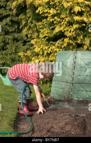 Ragazzo giocando con tubo flessibile facendo una pozza di fango e nel giardino sul retro. quattro-anno-vecchio Foto Stock